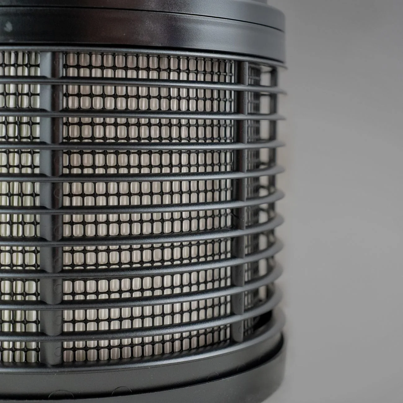 Texto Alternativo (Alt Text): Close-up da grelha de ventilação cilíndrica e do sistema de filtragem de um purificador de ar FilterQueen Defender em tons de preto e cinzento.
