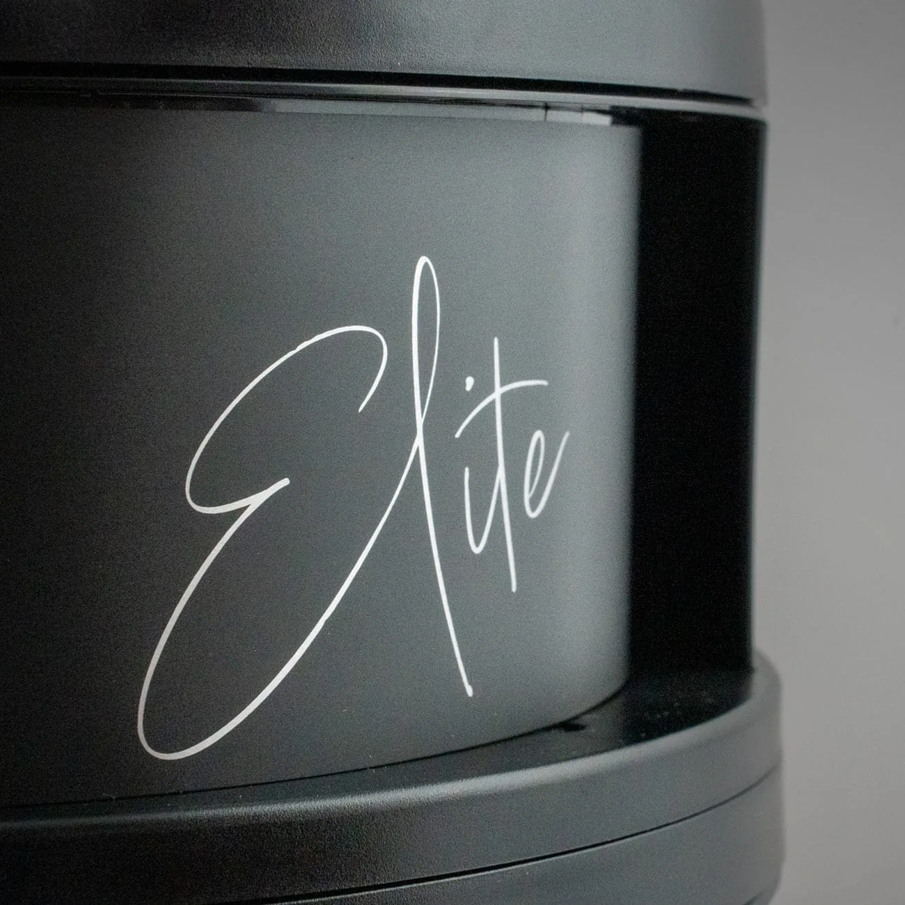 Close-up da inscrição "Elite" em letra cursiva branca sobre o corpo preto mate do purificador de ar Filter Queen Defender.